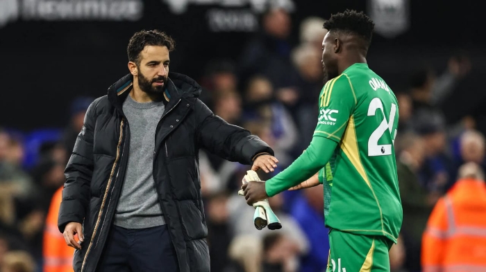Kiper Manchester United, Andre Onana (kanan), berjabat tangan dengan seorang pria berjaket tebal di lapangan sepak bola.
