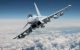 Sebuah pesawat tempur Eurofighter Typhoon berwarna abu-abu terang terbang dengan sayap sedikit miring ke bawah, dengan latar belakang langit biru cerah dan awan putih.